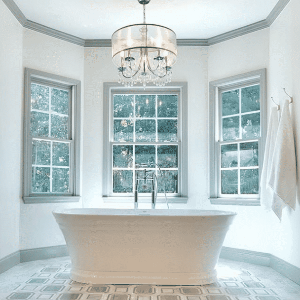 A large bright bathroom with 3 windows, chandelier and large white tub with walls painted in origami white sw 7636 by @design_build_sell_ga.