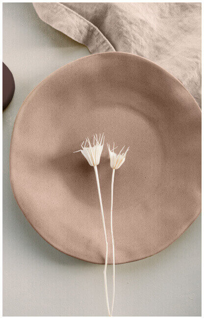 Two white flowers sitting on top of a tan ceramic plate and cloth napkin