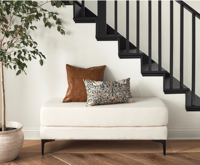 A white upholstered bench in a white entryway with a black staircase.