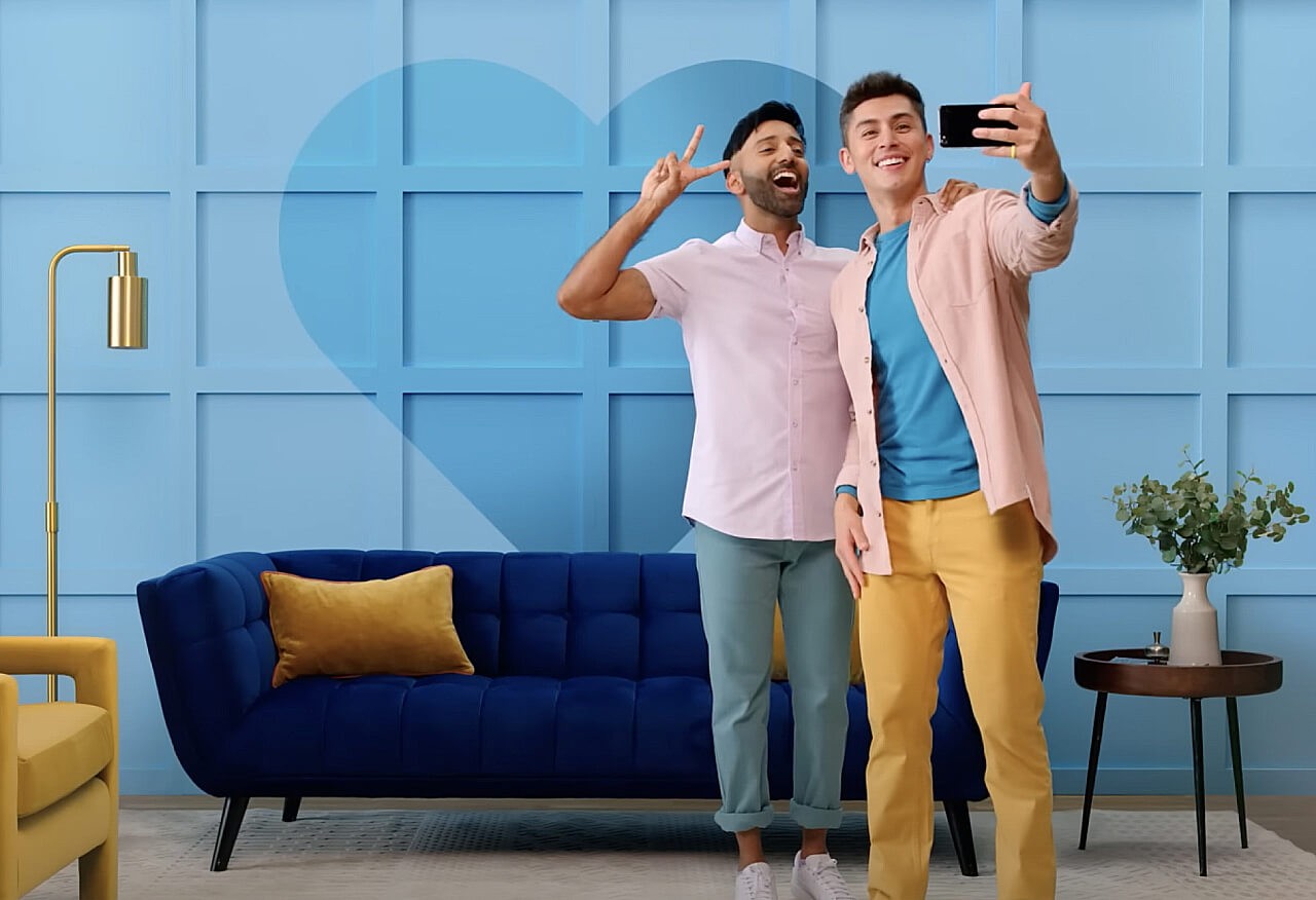 Two people taking a selfie together in front of a blue wall with a darker blue heart on it