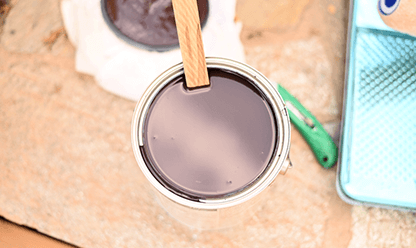 A open can of dark stain with a stir stick in the can.