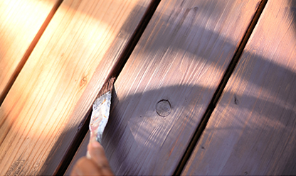 A person applying stain between deck boards with a brush