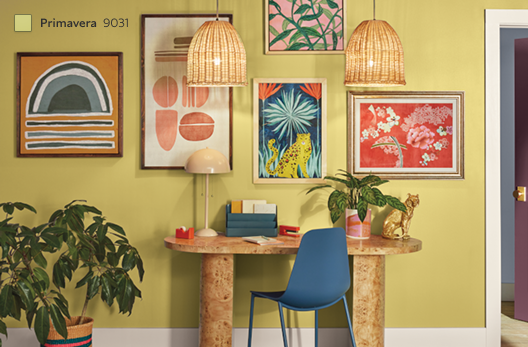 A gallery wall painted in SW 9031 Primavera with bright patterned art prints and an oval desk.