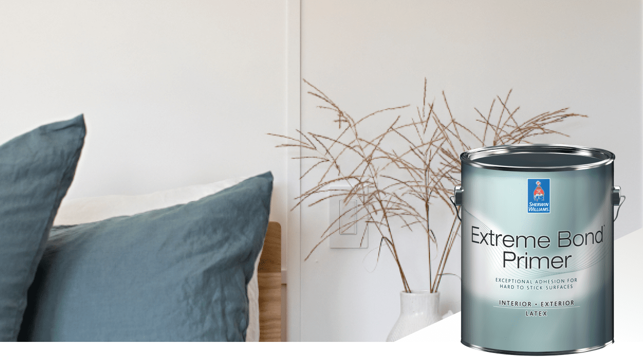 A white wall with a vase of brown stems in front of it alongside blue-gray pillows on a chair all with a can of Extreme Bond Primer.