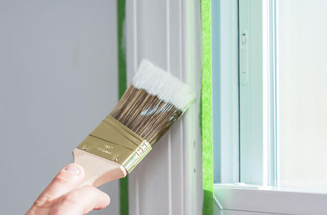 A painter painting window trim taped off with FrogTape® Multi-Surface Painter's Tapea using a small paint brush.