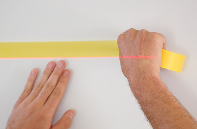 Two hands placing FrogTape® Delicate Surface Painter's Tape on a wall in a straight line.