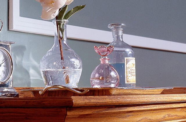 Wood dresser with a clock and three glass vases on top of a metal tray.