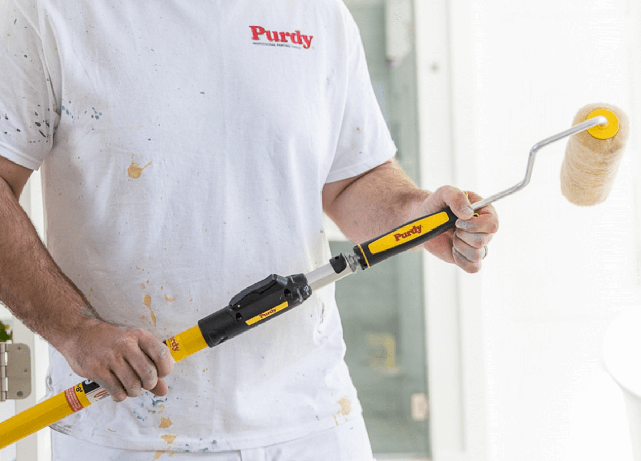 A person with a white shirt with the Purdy logo painting with a Purdy Roller.