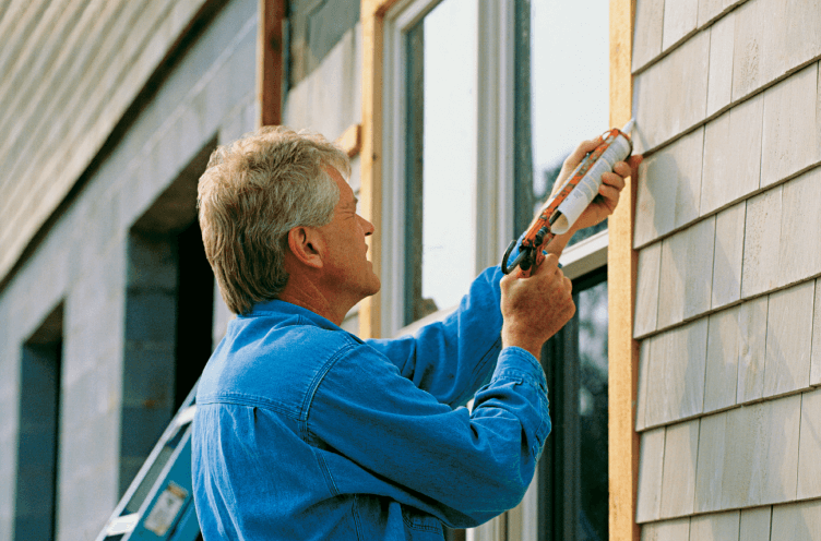 A person applying caulk to exterior window trim.