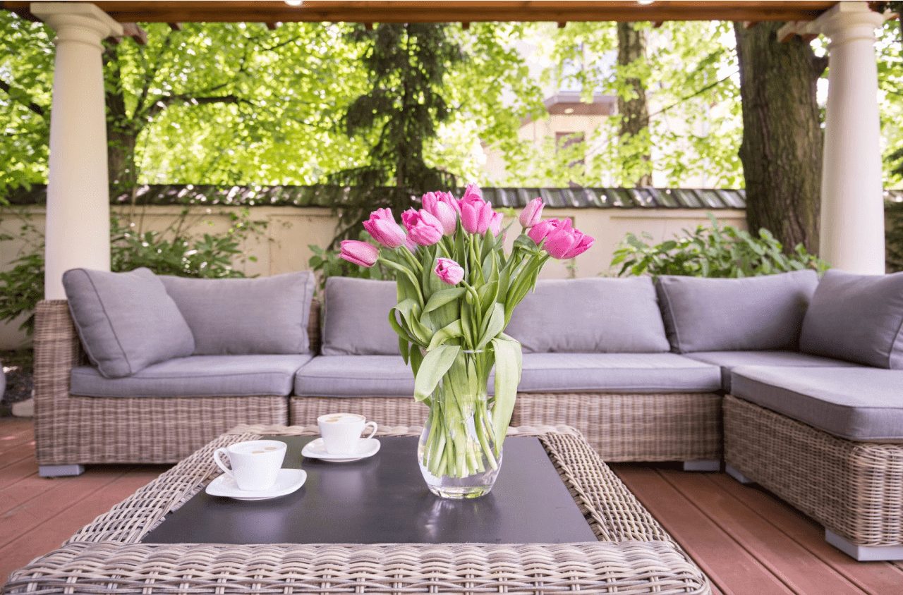 A large deck with a couch and cushions, table with cups and a vase with flowers.