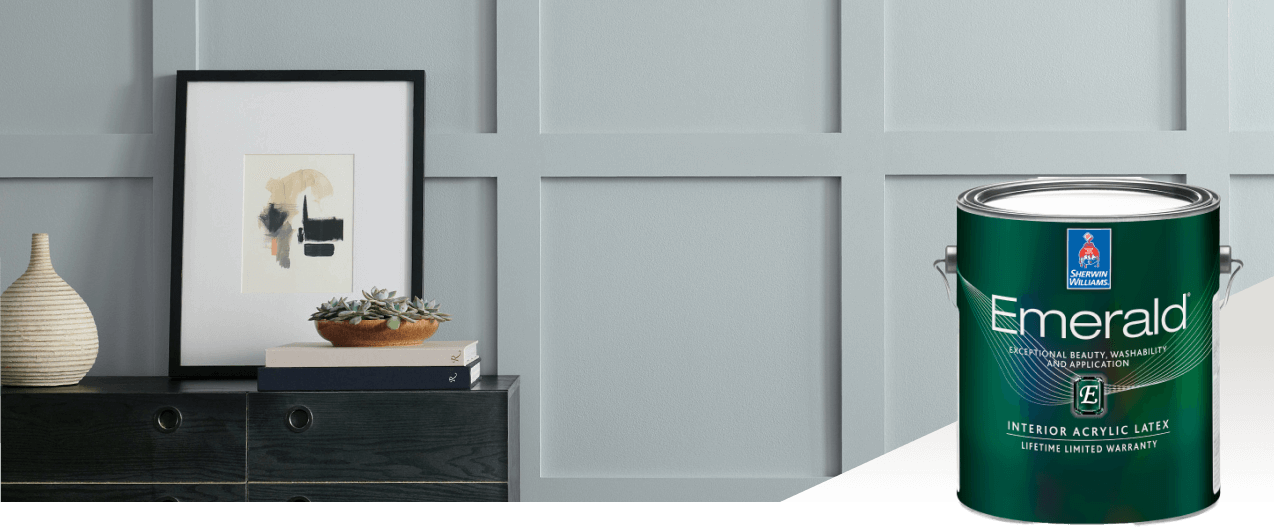 A light gray batten wall with wooden drawers in front with a picture resting on top. Featured product Emerald Interior Acrylic Latex.