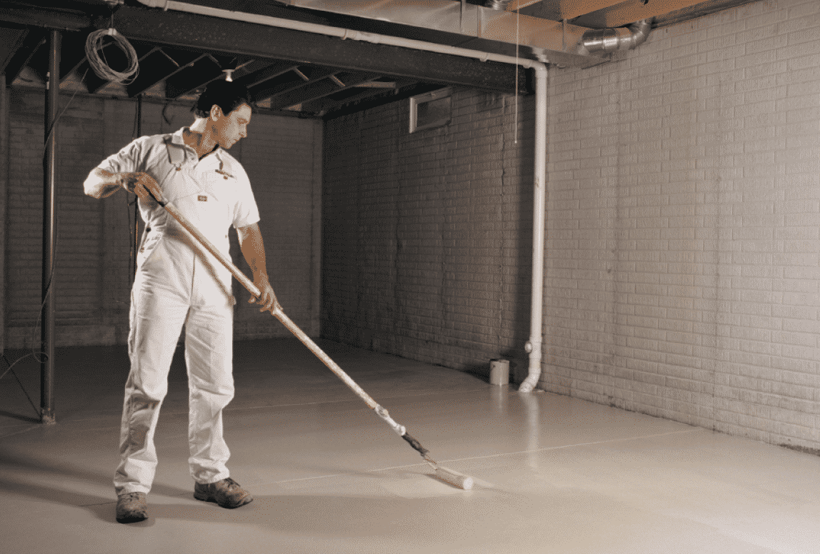 A person using a pole to roll stain on a concrete basement floor.