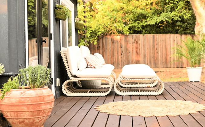 Outdoor patio deck with neutral furniture, rug, and plants.