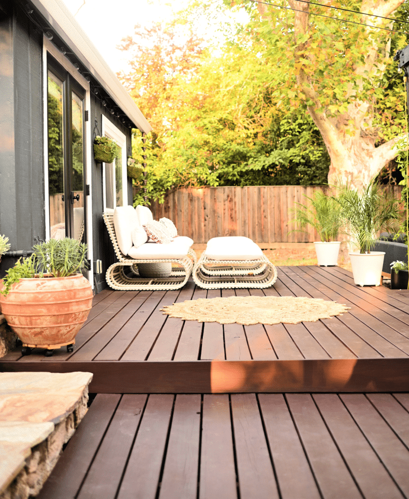 A wood deck with white patio furniture and a gold mat with potted plants.