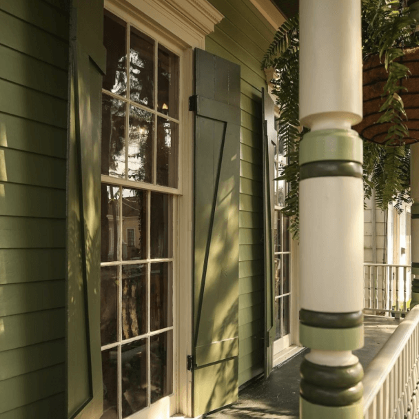 A house with a wrap around porch with large windows and wooden shutters painted in SW 2812 rookwood jade as well as the siding and column.
