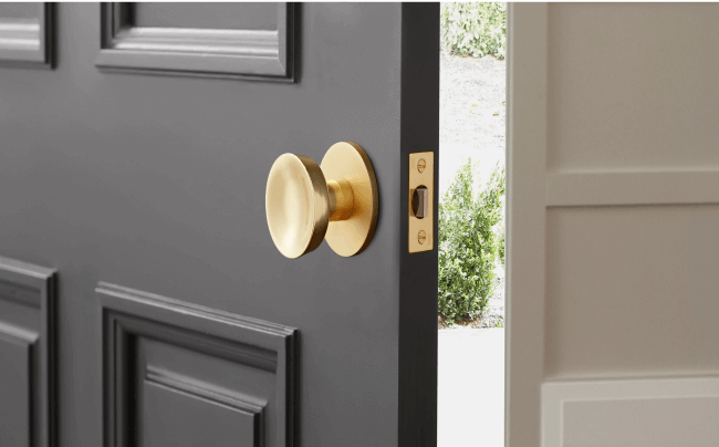 A foyer of a home with an open black door with a gold handle. Wooden floors with a rug and white walls.