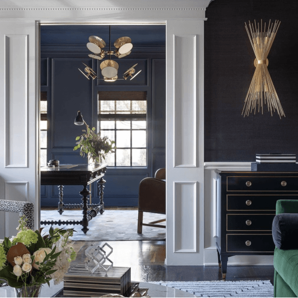 A living room with white door trim and navy blue walls that leads into an office.