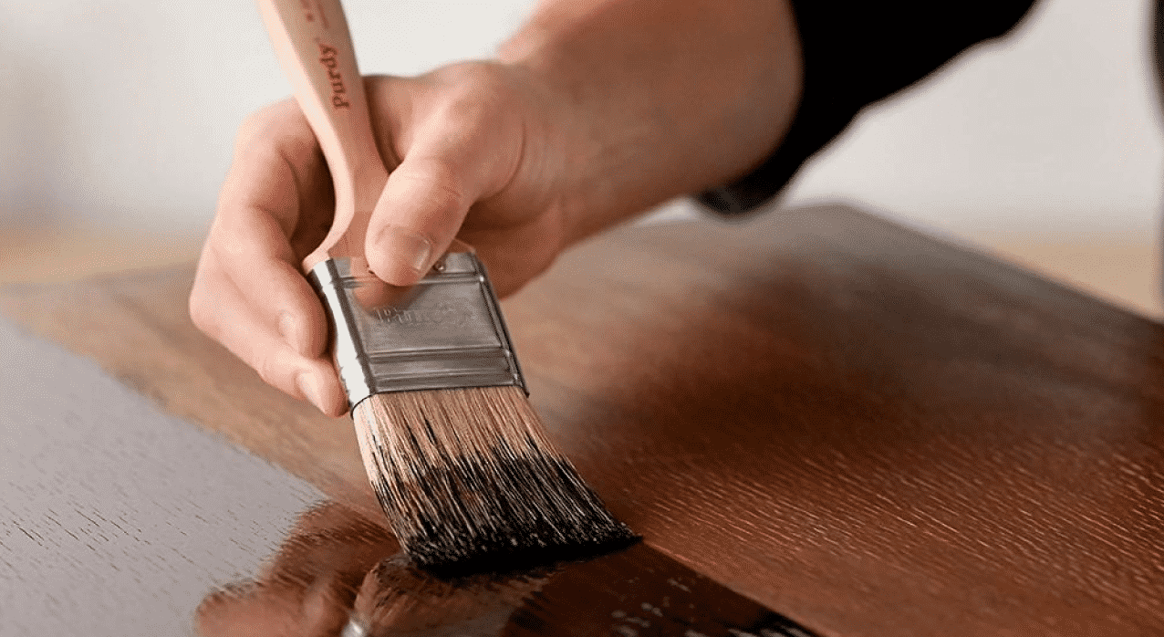 someone using a paint brush to stain a piece of wood.