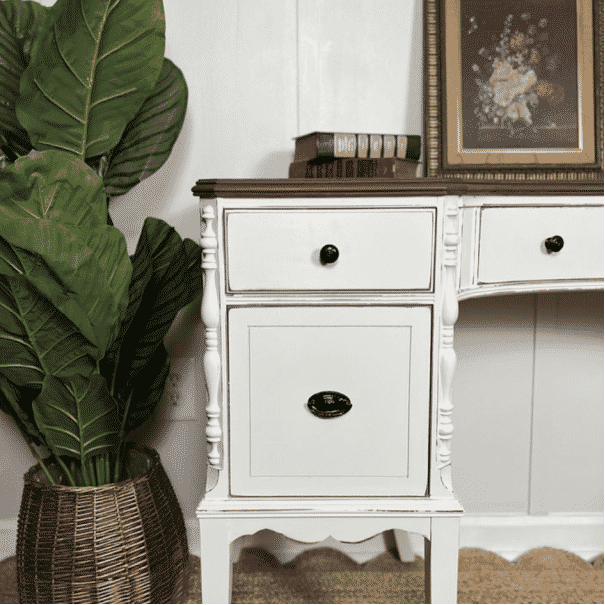 A white dresser with a picture and book on top of it next to a green plant, by theivyandbirch.