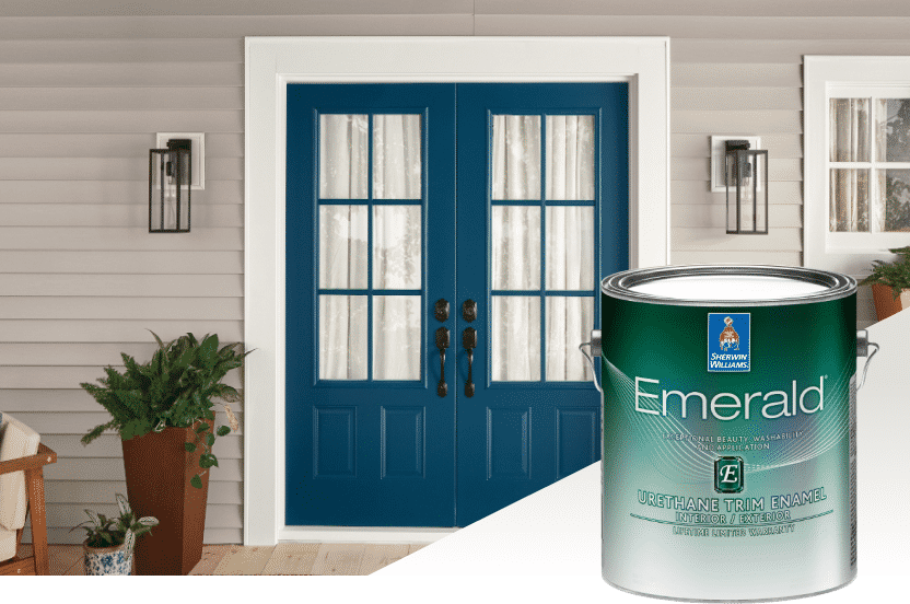 A can of exterior Emerald paint set in front of double front doors painted blue with a potted fern to the left side and an outdoor chair.