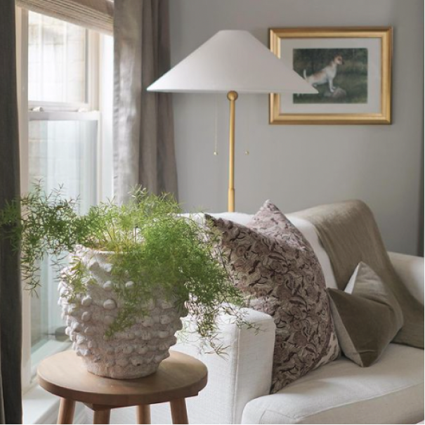 Living room painted in morning fog with neutral loveseat, plant, lamp, and picture frame, by @stayhomestyle_.