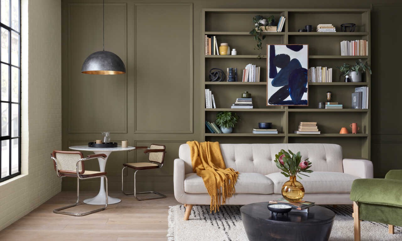 A modern living room with a built in bookshelf painted the same dark olive color as the walls.