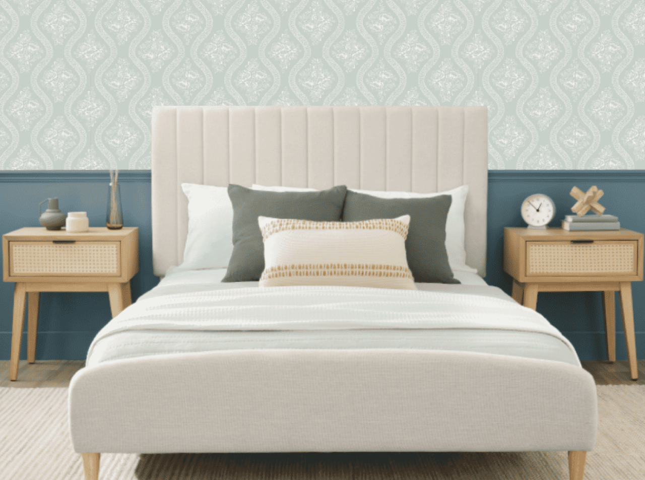 A large bed with neutral colors with twin light wooden nightstands on each side in front of a wall with light green wallpaper.