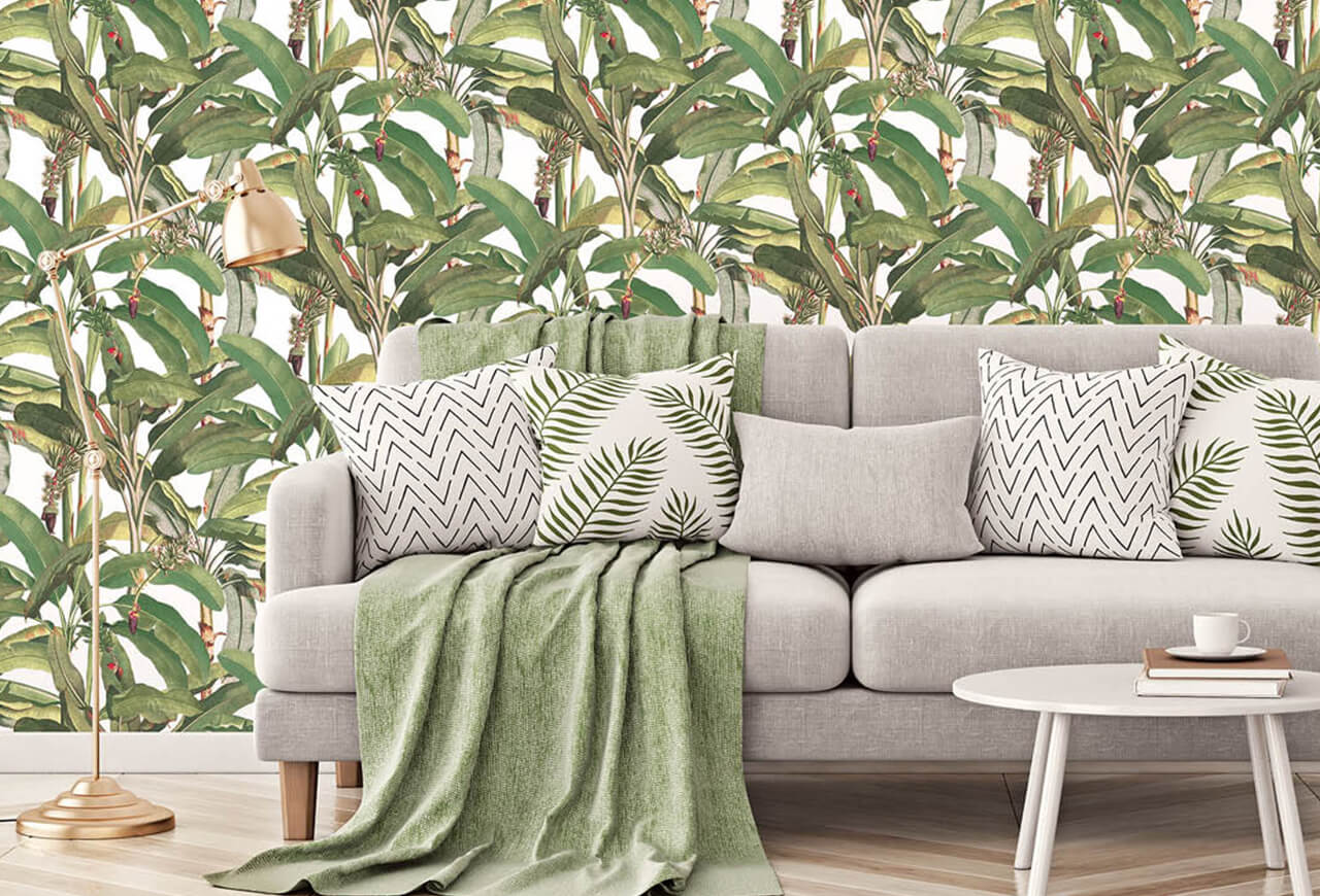 A gray cloth sofa in front of a wall with green botanical wallpaper.