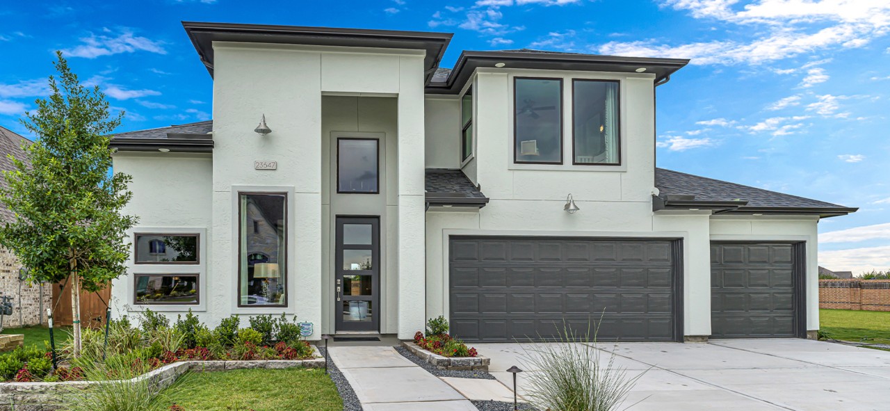 Contemporary-design home exterior with large rectangular windows, two-door garage, and two-story grand entrance in front of blue sky.