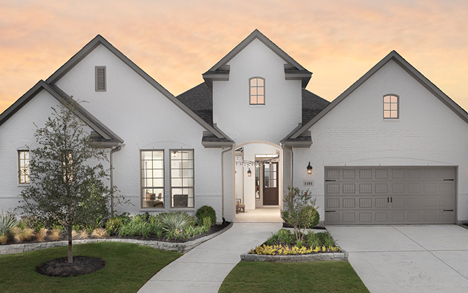 Street view of new home painted white with steep gables, attached garage, and lush landscaping at sunset.