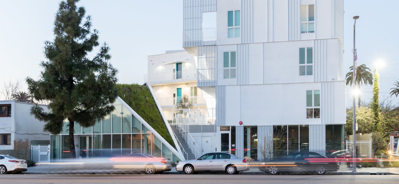 Exterior shot of white modern four-story apartment building with wedge of green space extending down from the roof to street level.