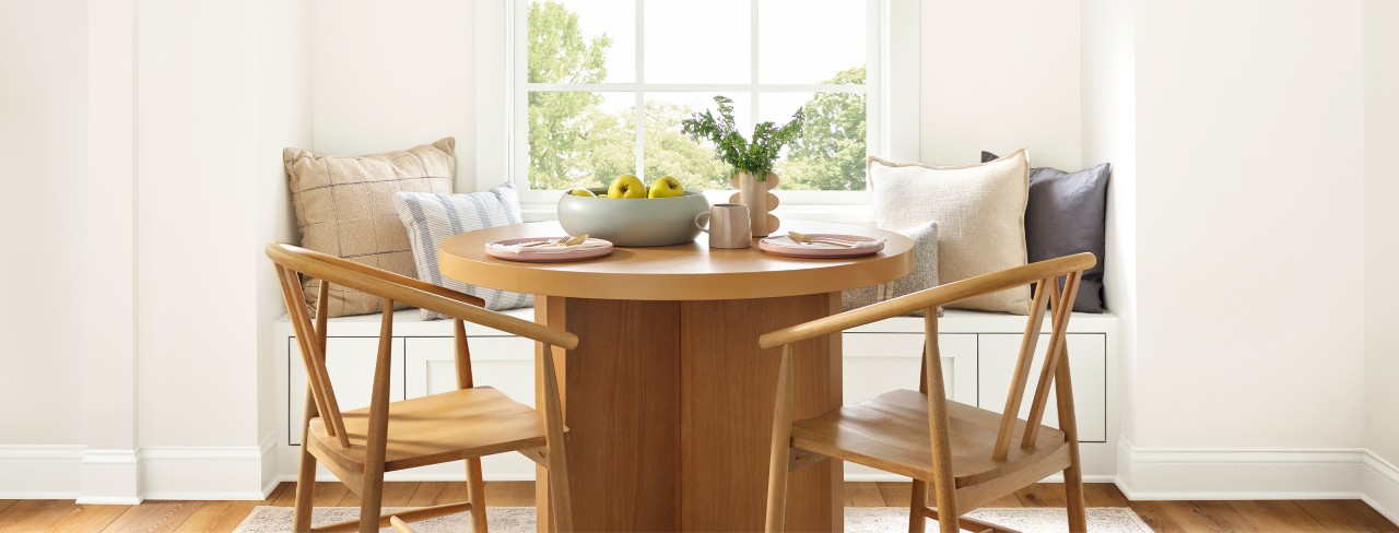 Naturally lit dining nook area with wood table and chairs in front of a window bench seat.