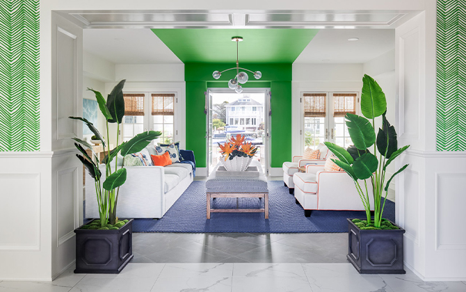 Living room with white sofa and armchairs, blue rug, and white walls and ceiling with bright green painted stripe down the center of the room, twin potted palms in foreground.