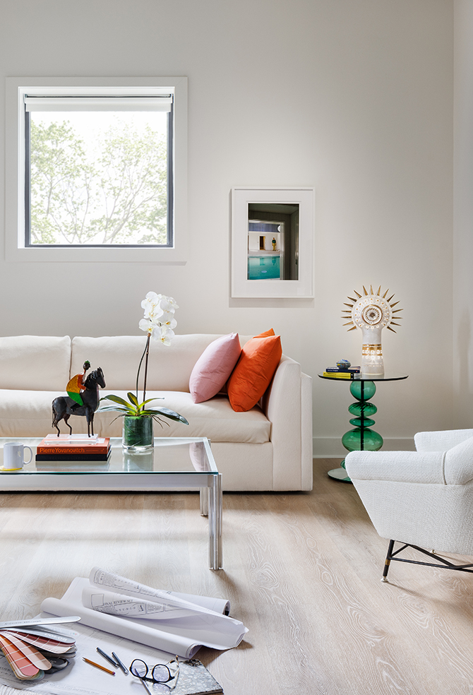 A modern sitting room in designer Seth Van Den Bergh’s studio with white furniture and colorful accents, including books, a sculpture, and an orchid on a glass table, painted Westhighland White by Sherwin-Williams.