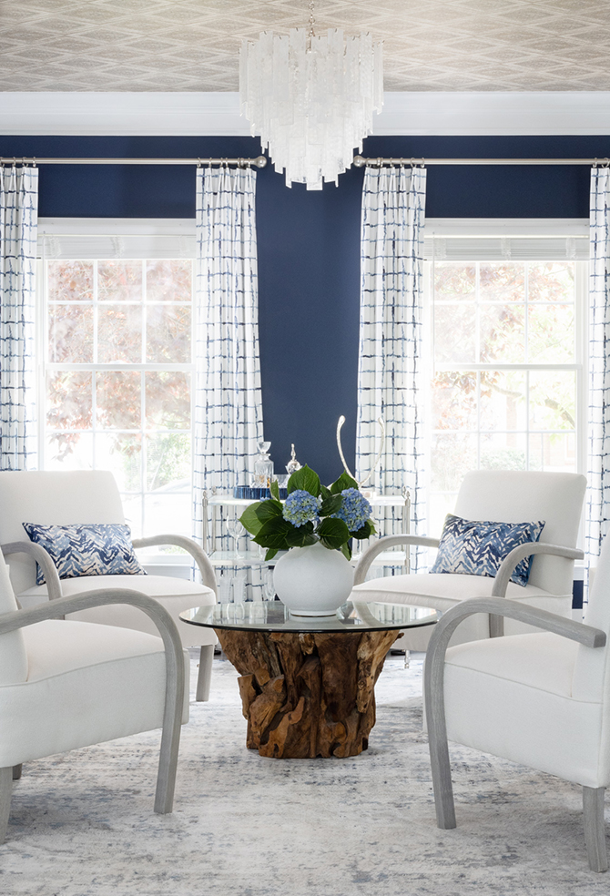 Modern living room with navy blue walls painted Distance by Sherwin-Williams, white armchairs, and blue hydrangeas on a wooden coffee table.