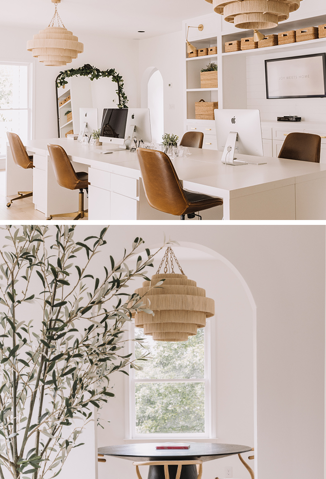Modern office space with white desks and brown leather chairs, featuring iMac computers, large chandeliers, and built-in shelving.