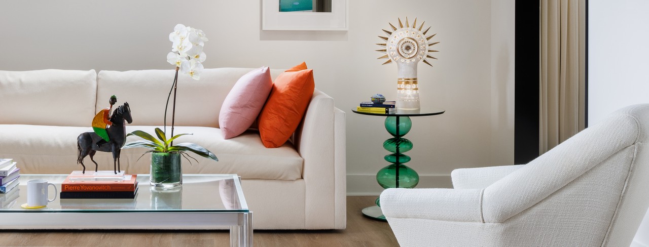 A modern sitting room in designer Seth Van Den Bergh’s studio with white furniture and colorful accents, including books, a sculpture, and an orchid on a glass table, painted Westhighland White by Sherwin-Williams.