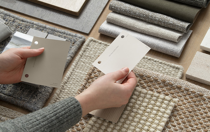 Fabric and textile swatches in a neutral color scheme and hands holding sample color chips in Sherwin-Williams colors Quarry Stone and Drift of Mist.