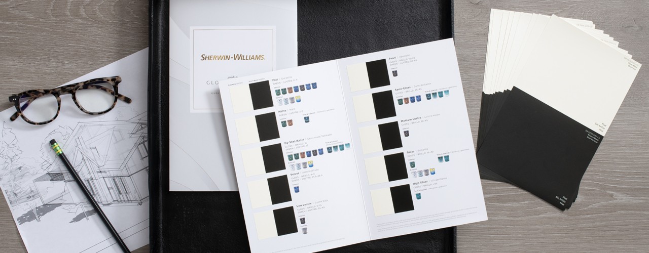 Flat lay with architectural drawing, the Guide to Gloss & Sheen laid open on a blotter, tortoiseshell eyeglasses and sheen samples fanned on a desktop.