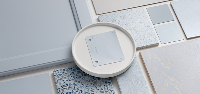 Flat lay featuring various substrates coated using the Sherwin-Williams gray-blue color: Upward, with a color sample chip on a small white plate in the center.