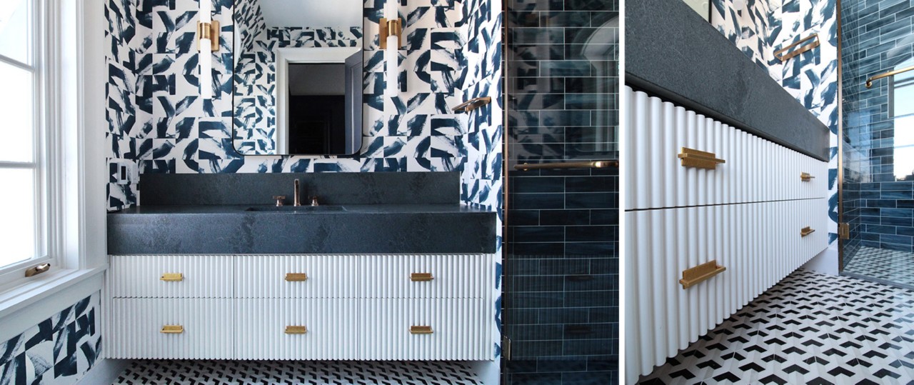 Full view and angled closeup of fluted white vanity with dark countertop and bold patterned wallpaper, dark blue tiled walk-in shower at right.