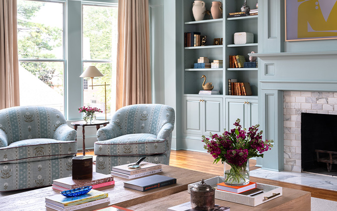 Light blue-green painted living room with matching round back arm chairs near tiled fireplace.