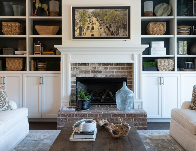 Inviting living room with brick hearth, built-ins full of baskets and accessories, and comfortable sofas with wood coffee table in the foreground.