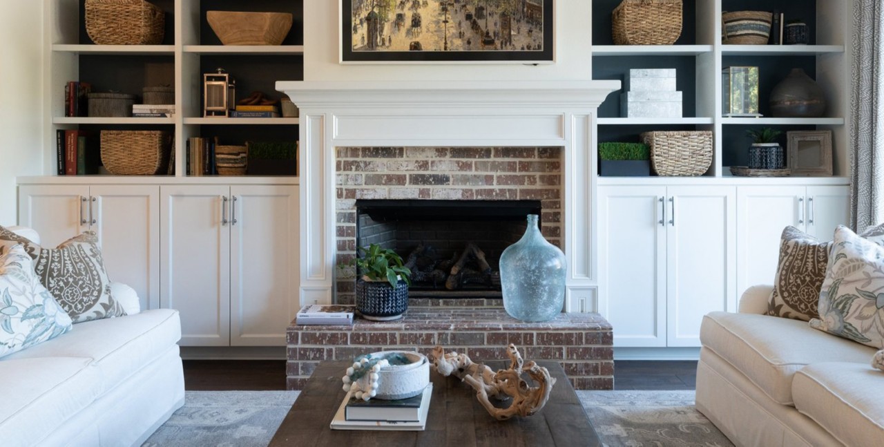 Inviting living room with brick hearth, built-ins full of baskets and accessories, and comfortable sofas with wood coffee table in the foreground.