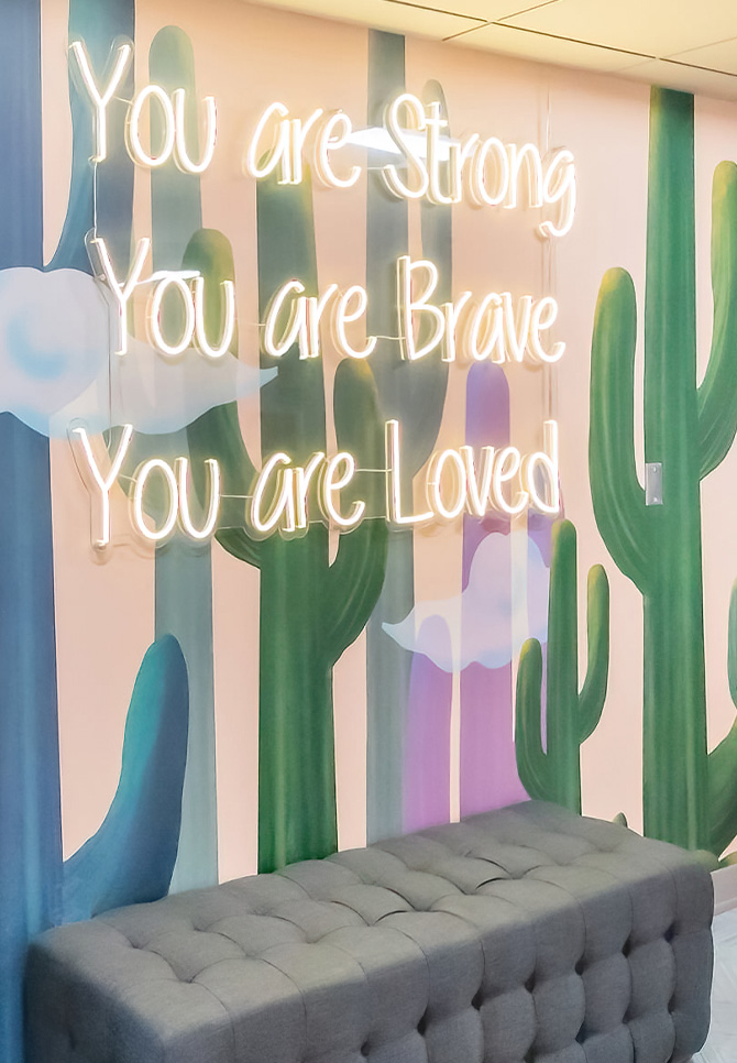 Tufted bench in front of an art-panel wall with an inspirational phrase neon sign.