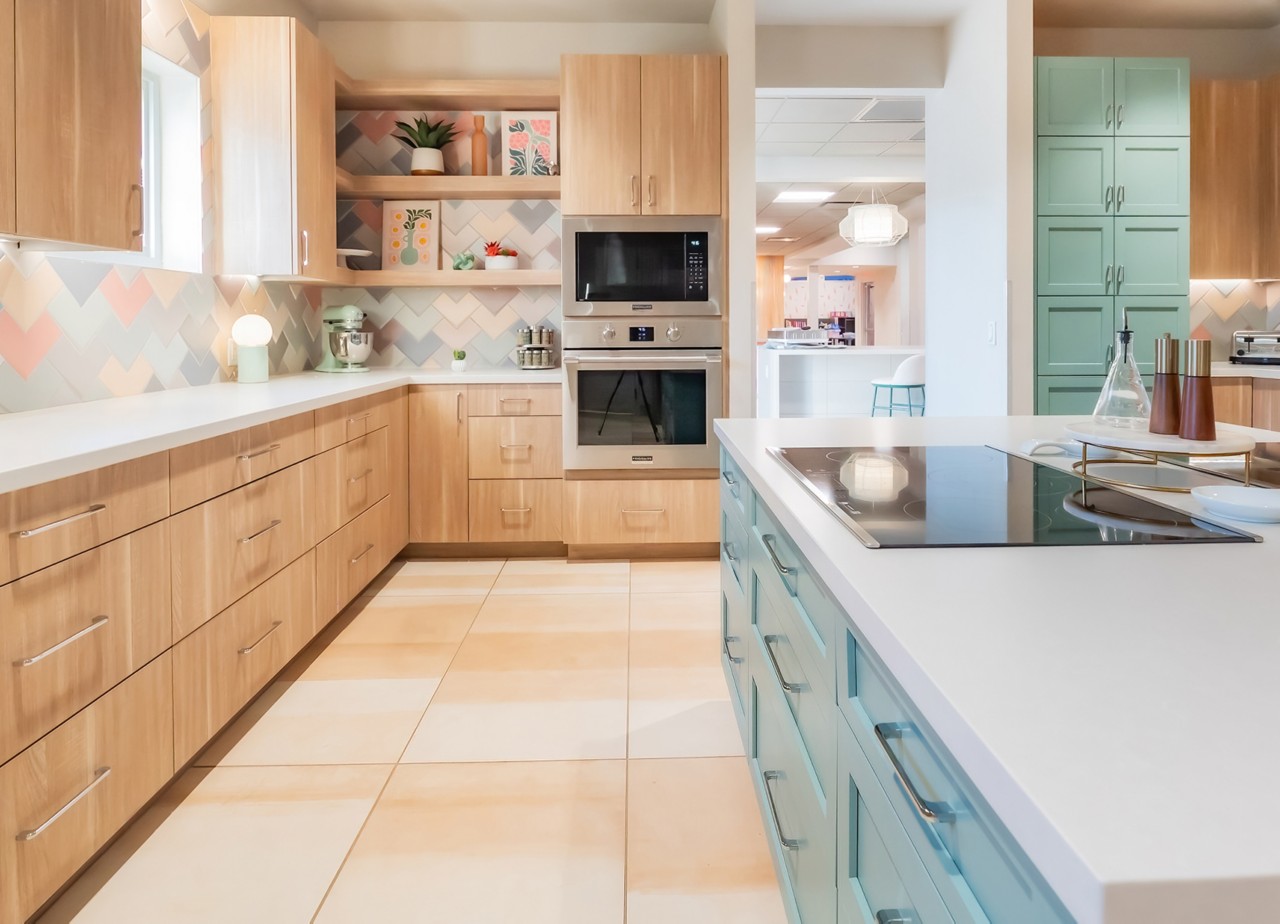 Spacious community kitchen in the Ronald McDonald House with wooden cabinets around the perimeter, accent and island cabinets painted Jasper Stone by Sherwin-Williams, new appliances, and pastel chevron backsplash.