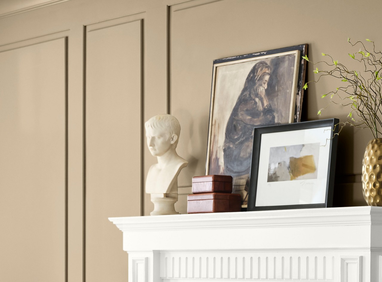 Decorative items on a white mantel against a paneled wall painted Universal Khaki, including a marble bust, artworks, and a gold vase with a branch.