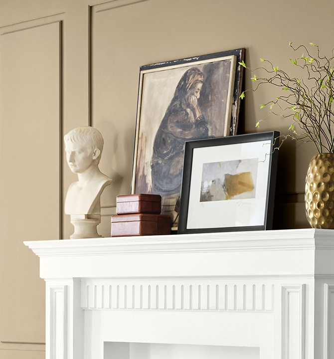 Decorative items on a white mantel against a paneled wall painted Universal Khaki, including a marble bust, artworks, and a gold vase with a branch.