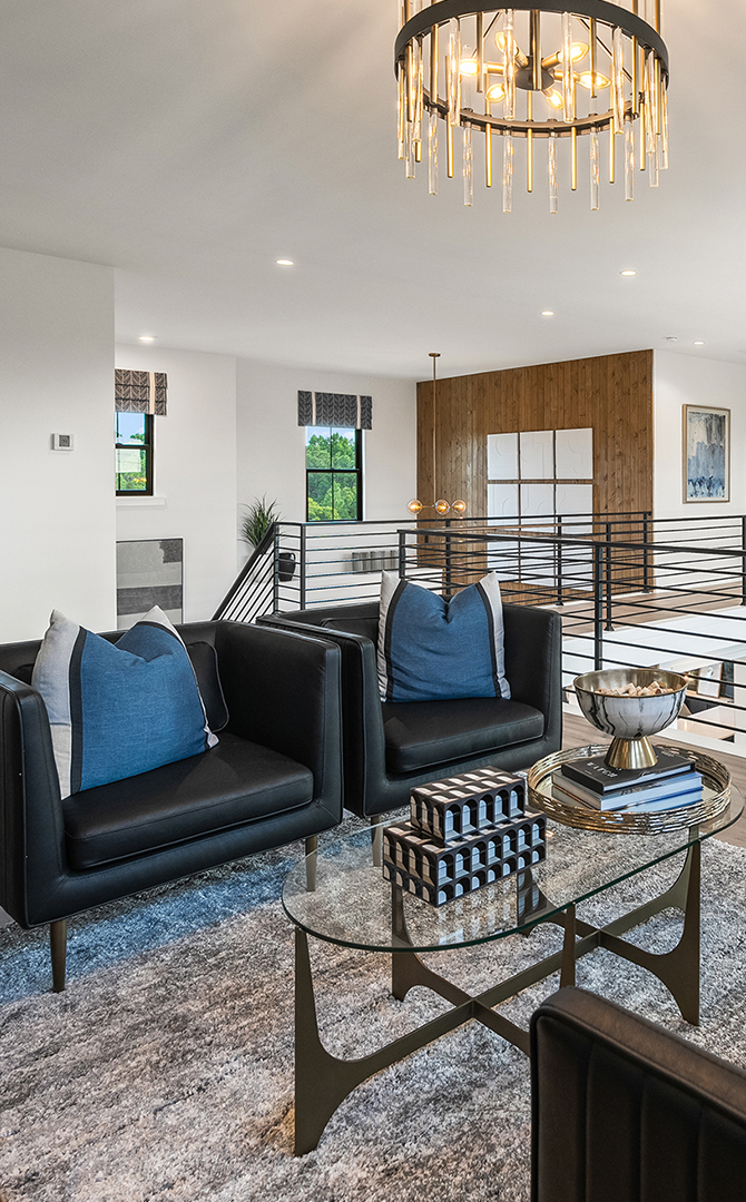 Lounge area in the upstairs landing of a modern home featuring black armchairs, a glass coffee table, and a decorative chandelier with walls painted Pure White by Sherwin-Williams.