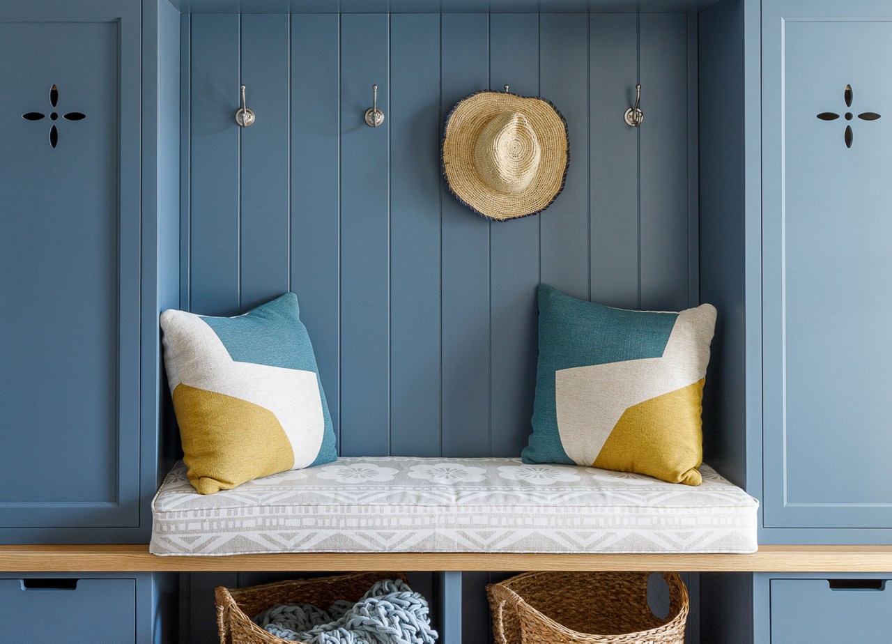 Detail shot of a cushioned bench, decorative pillows, hooks, and baskets in a built-in painted blue using Sherwin-Williams Stargazer.